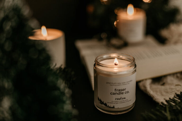 pumpkin scented soy wax candles lit on a table near some pine tree decoration and moody dim lighting